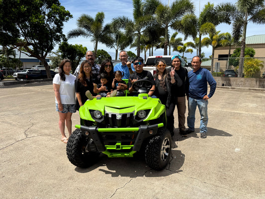 The Gardenland Hawaii team and family, including children, smiling proudly around a new bright green UTV (Utility Task Vehicle) on a sunny day in Maui, with palm trees and commercial buildings in the background.