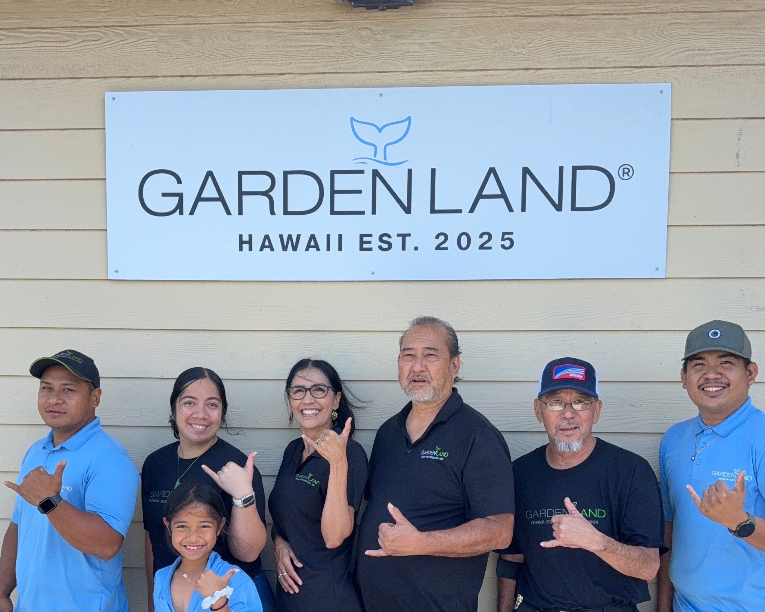 Group of people posing together in front of a 'Gardenland Hawaii' sign.